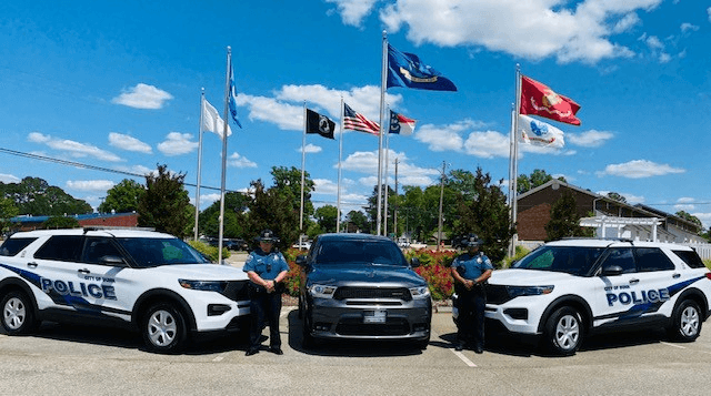 Dunn Police Department officers standing with patrol vehicles in front of the department flags